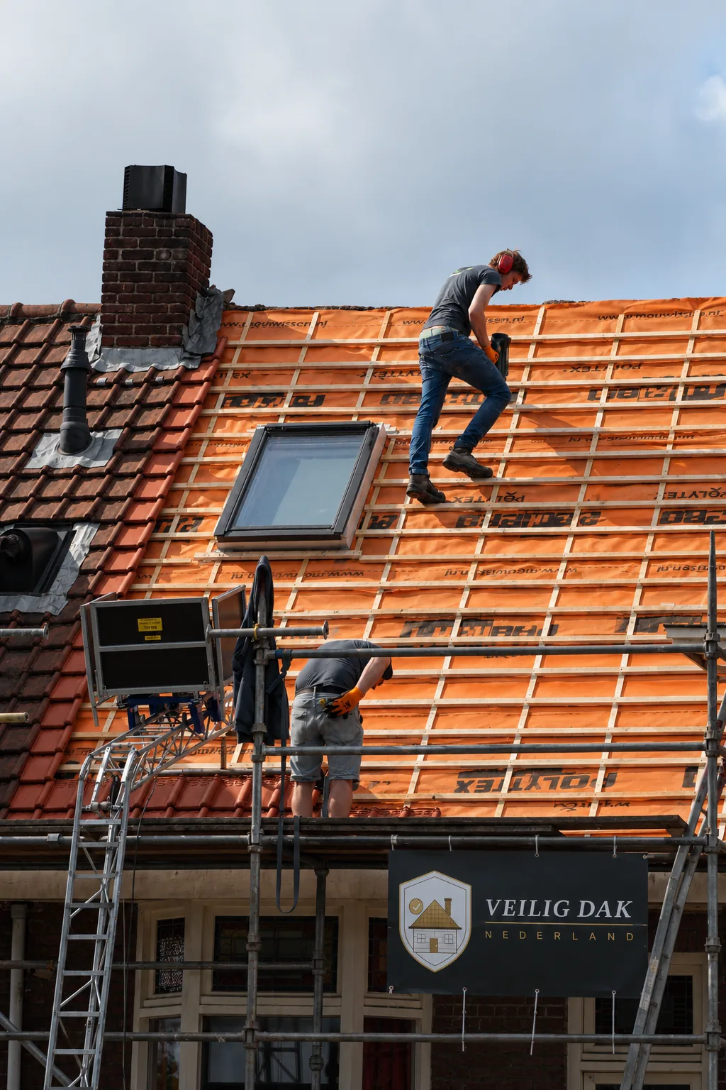 Twee dakdekkers van Veilig Dak Nederland aan het werk op een steiger